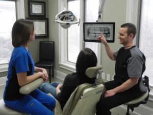 Dr. Patrick Singley explains a treatment plan to a patient in the operatory, while assistant Brandy Shelton is able to access digital radiography with DEXIS, and make clinical notes in Dentrix.